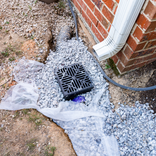 A drainage system is being installed on the side of a brick building.