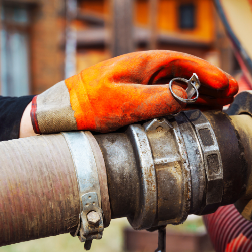 A person wearing orange gloves is holding a hose