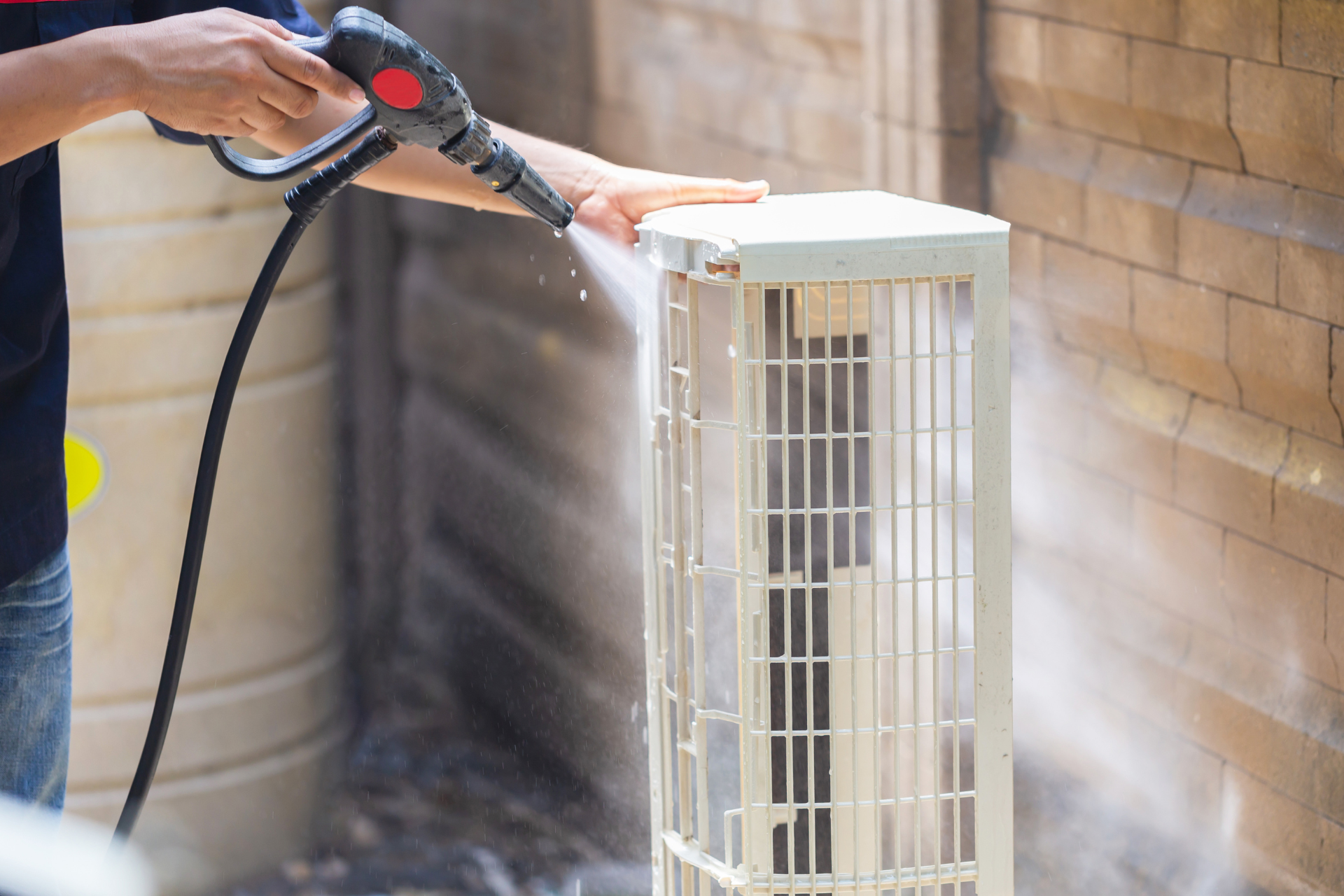 a person is cleaning an air conditioner with a high pressure washer .