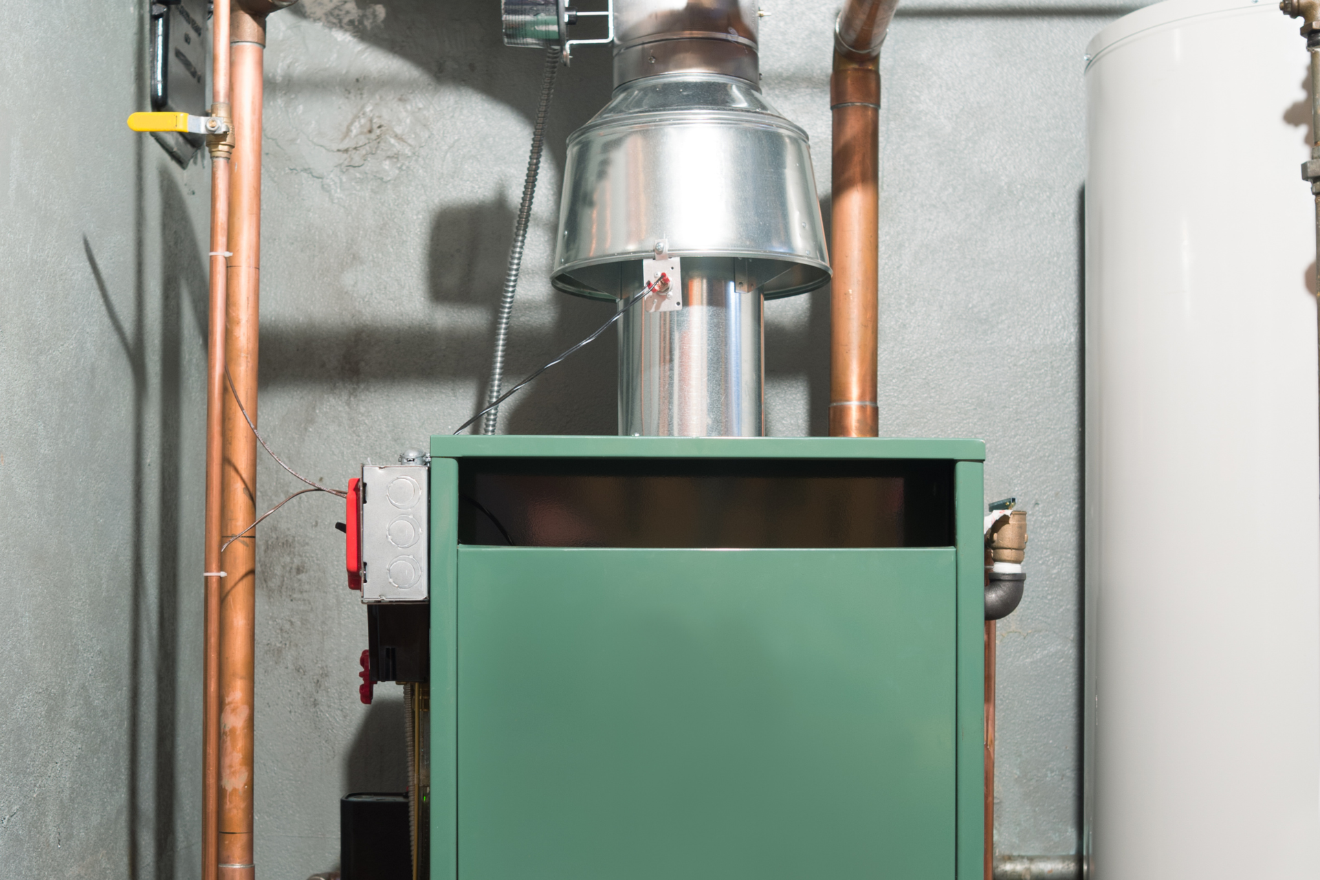 a green boiler is sitting in a room next to a water heater .