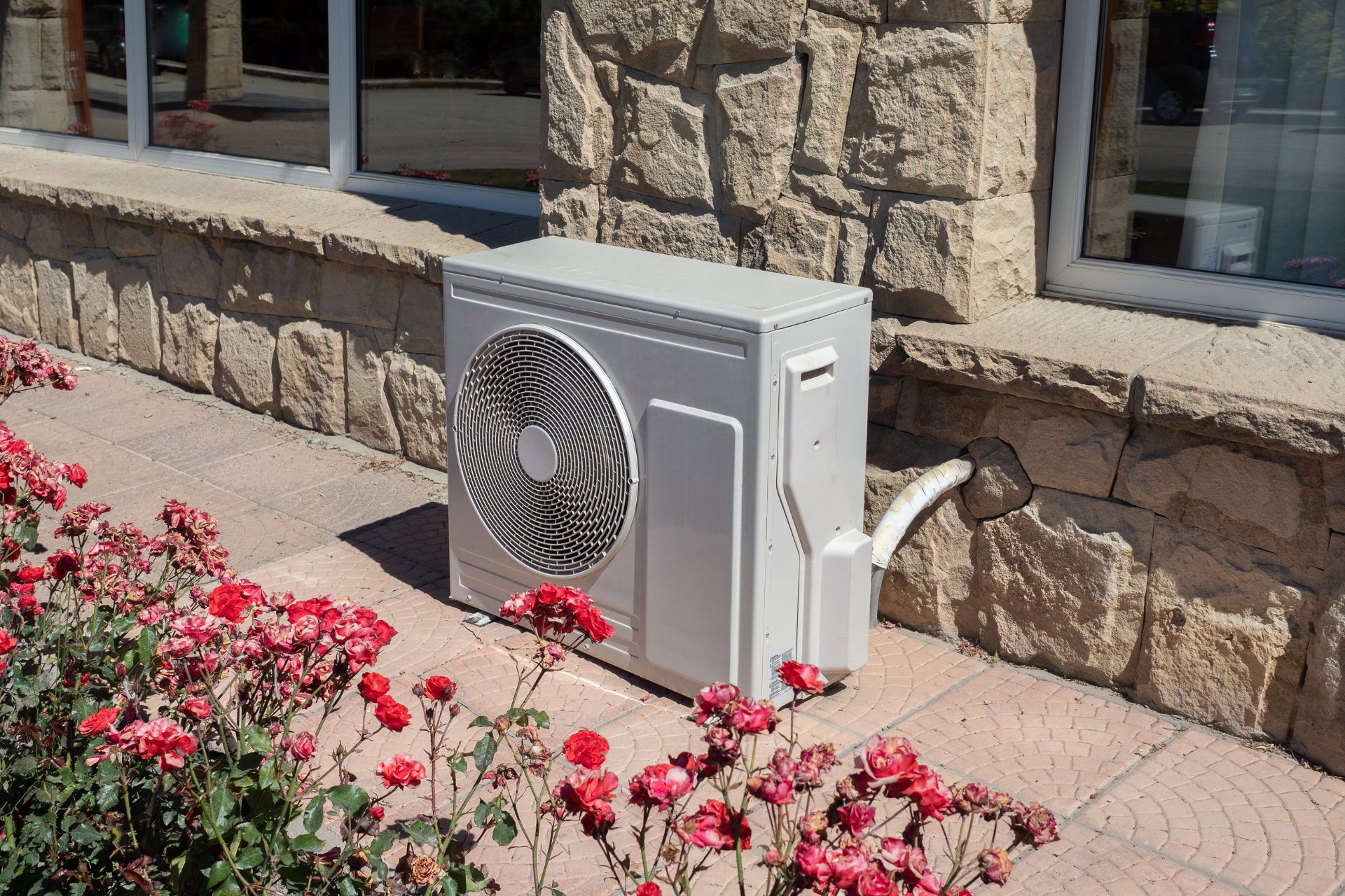 A white air conditioner is sitting on a sidewalk next to a stone wall.