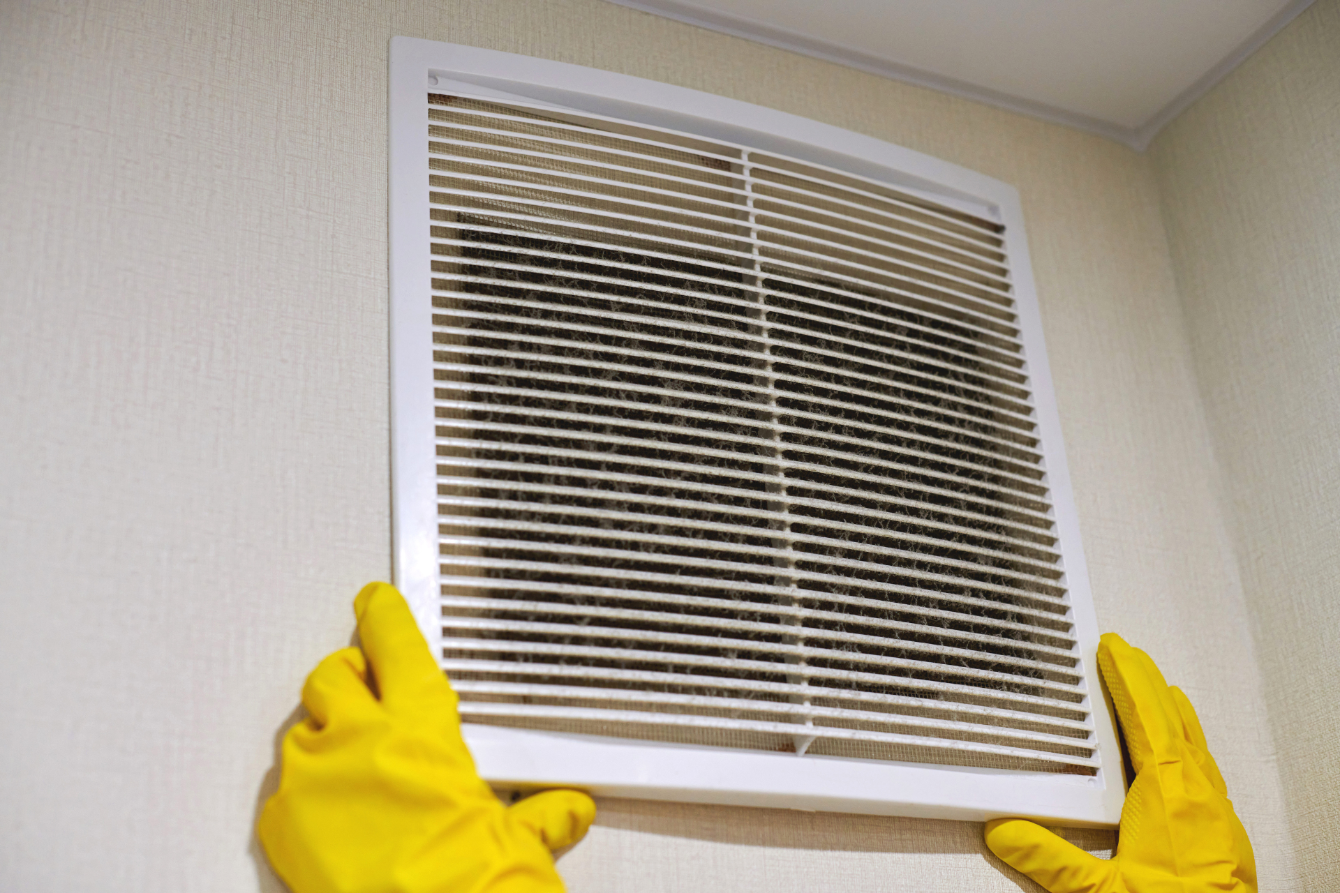 a person wearing yellow gloves is cleaning a vent on a wall .