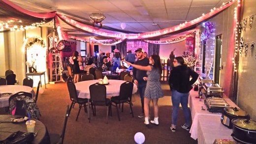 Party with decorated ceiling, people near tables. Pink and white decor, food station visible.