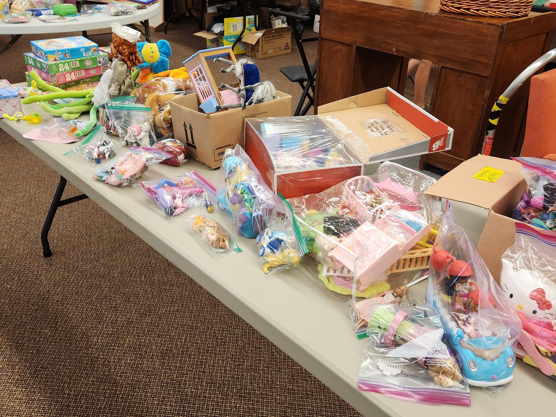 A table laden with toys and packaged items, likely at a sale or market.
