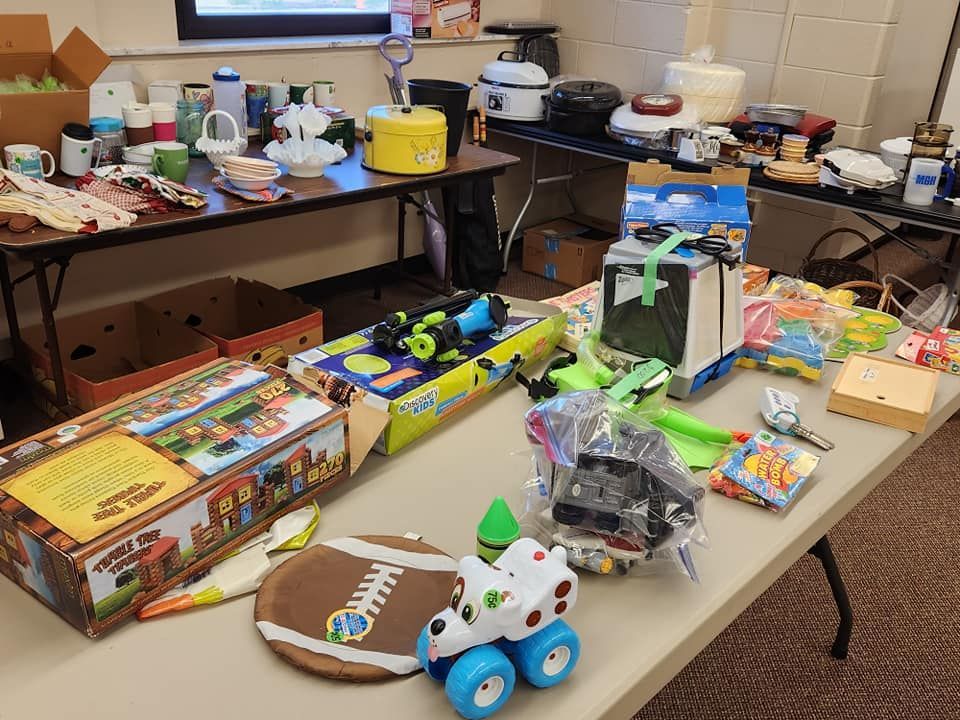 Tables displaying items for sale at a sale. Toys, kitchenware, and decorative items are visible.