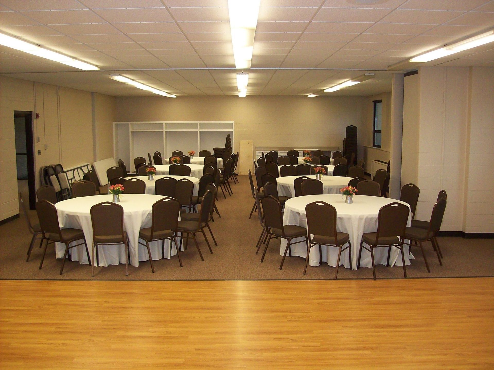 Banquet hall with round tables set for a gathering; brown chairs, white tablecloths.