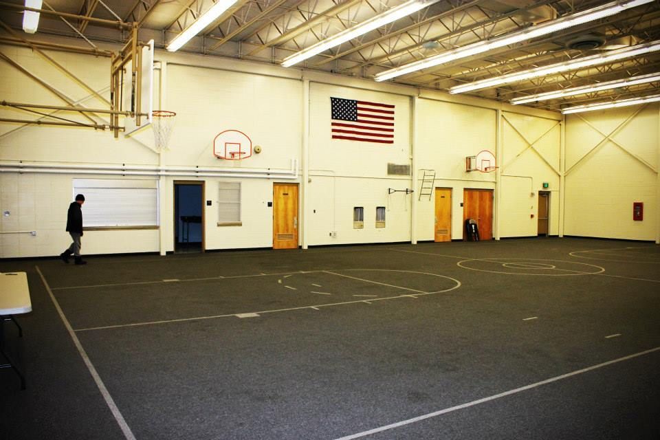 Gymnasium interior with basketball hoops, American flag, person walking.