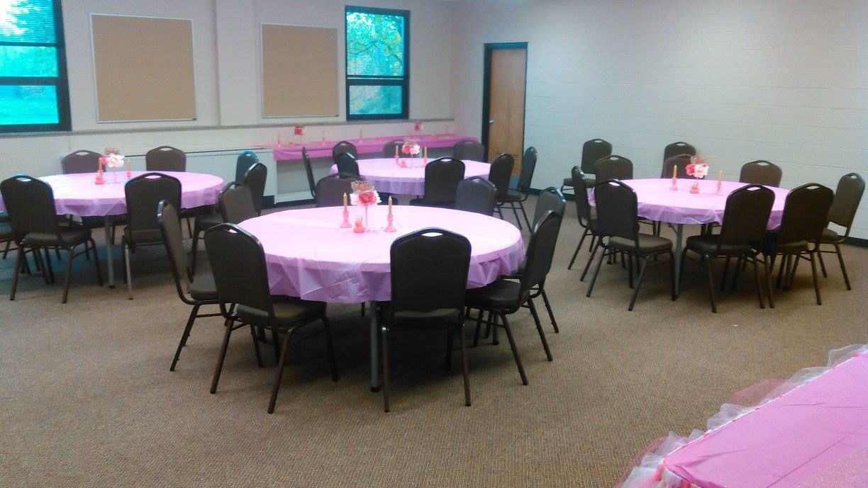 Round tables with pink tablecloths and black chairs set up in a room, ready for an event.