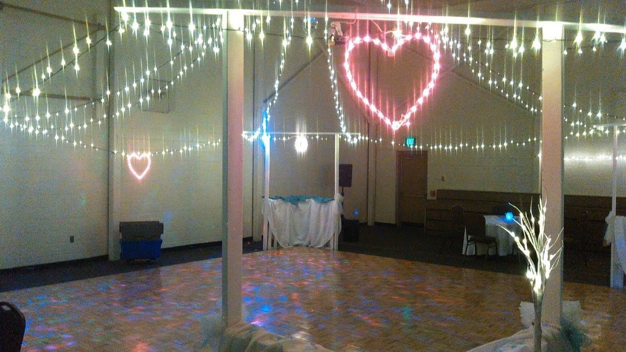 Reception hall decorated with string lights, heart-shaped lights, and a white-skirted table on the dance floor.