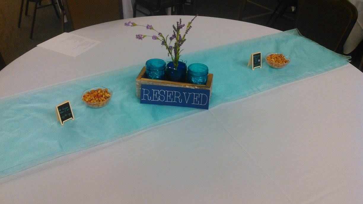 White round table with a teal runner. Centerpiece includes flowers, blue vases, and snacks.