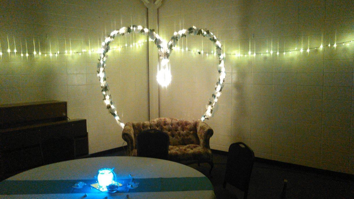 A decorated heart arch with string lights and a bulb, over a couch in a room. Table in foreground.