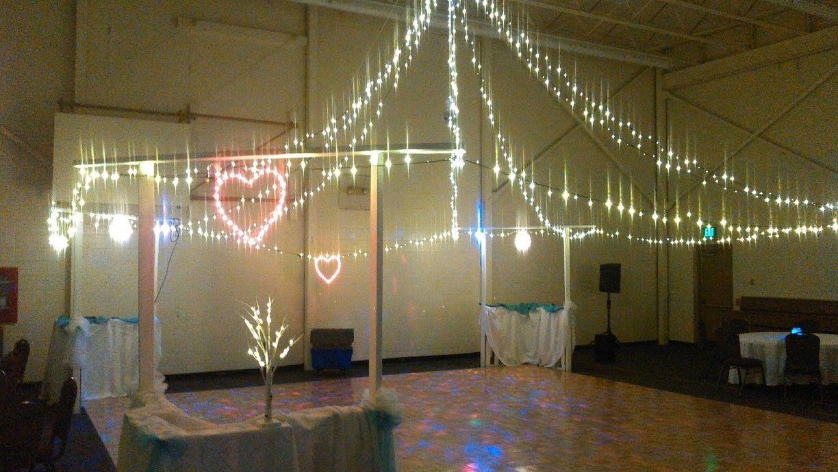 Event hall decorated with string lights, lit hearts, a dance floor, and a table with turquoise accents.