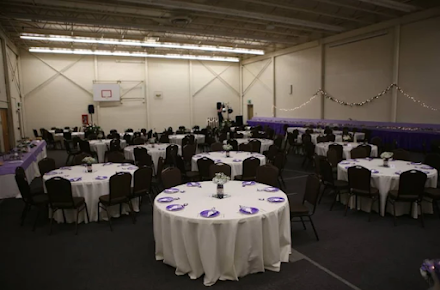 Reception hall with round tables set for a party, featuring white tablecloths and purple accents.