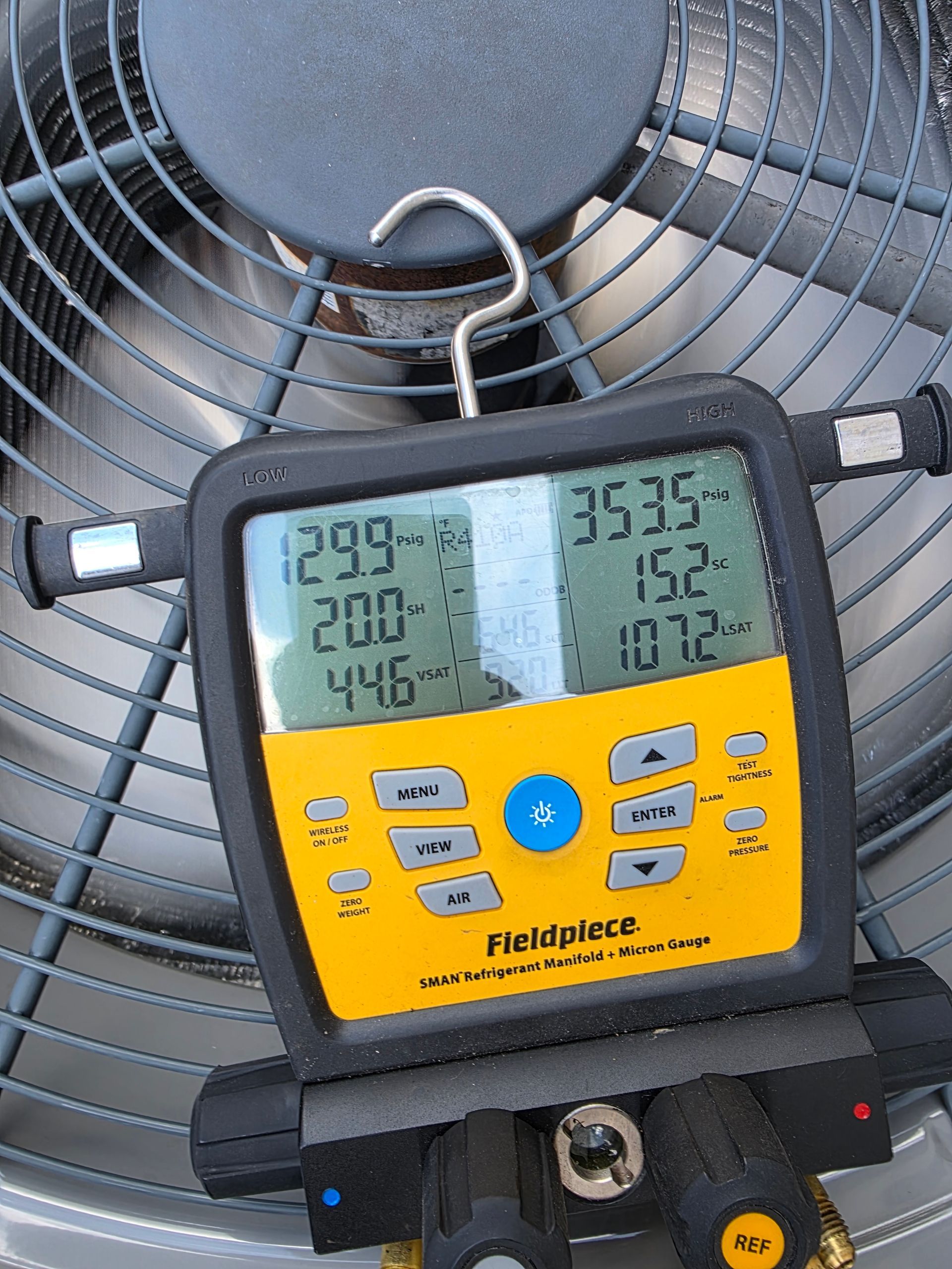 Two white HVAC units sit outside a light blue building, with windows and a brick wall.