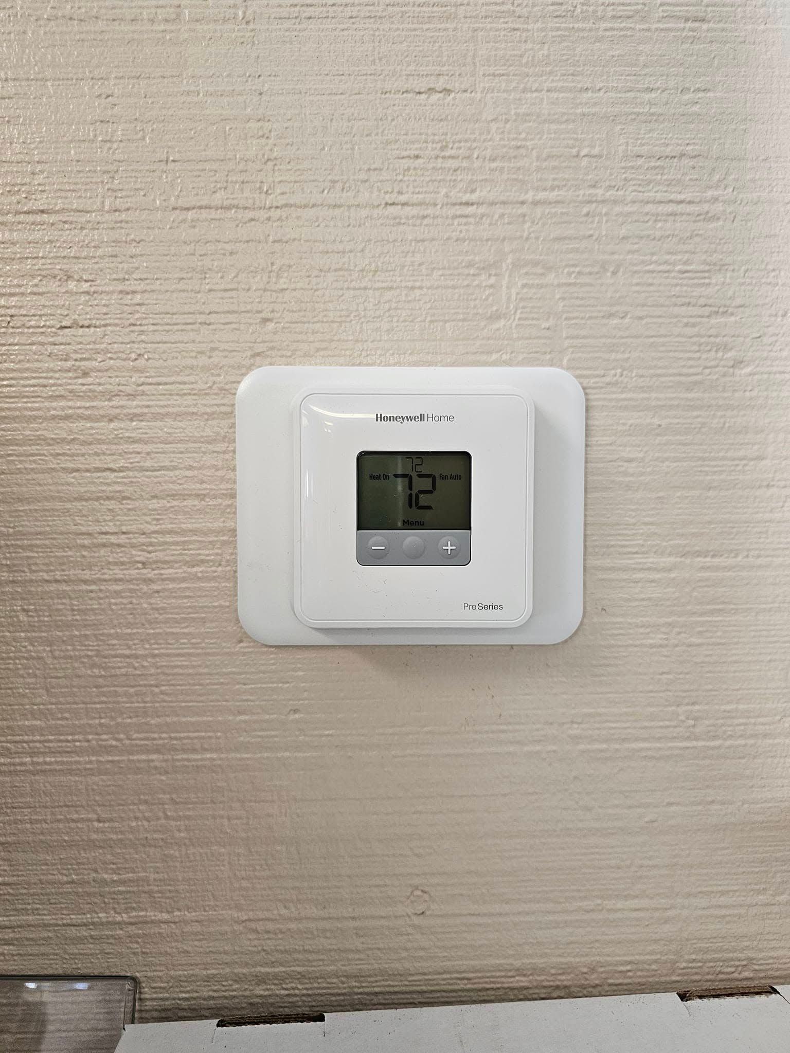 White thermostat on a textured wall, displaying a temperature of 72 degrees.