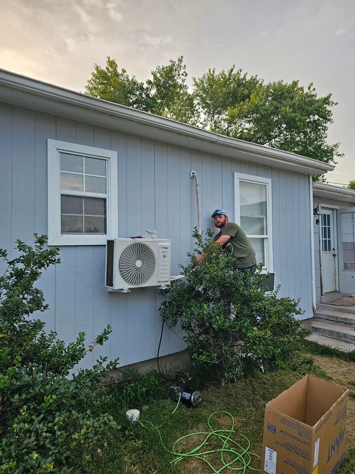A person installs an air conditioning unit on the side of a light blue house.