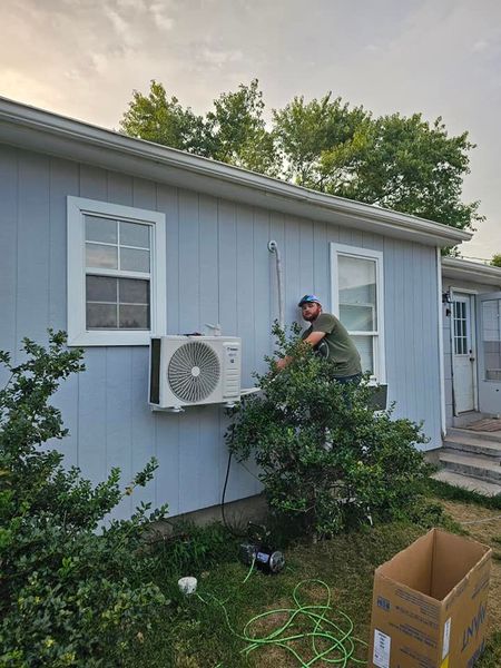 A person installs an air conditioning unit on the side of a light blue house.