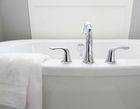 Chrome bathroom faucet and handles centered on a white bathtub with a white towel draped over the side.