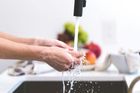Hands lathered with soap are being rinsed under a kitchen faucet with fresh fruit in the background.