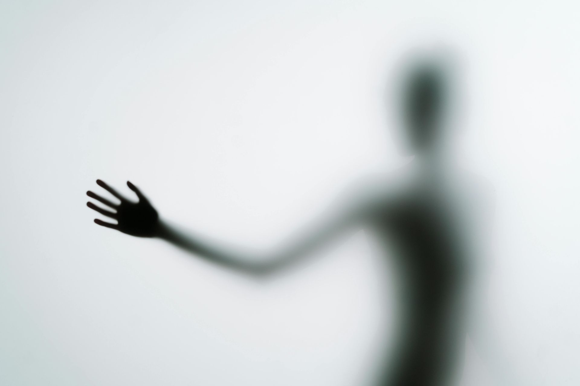Silhouette of a person reaching out, arm extended, against a white, blurred background.