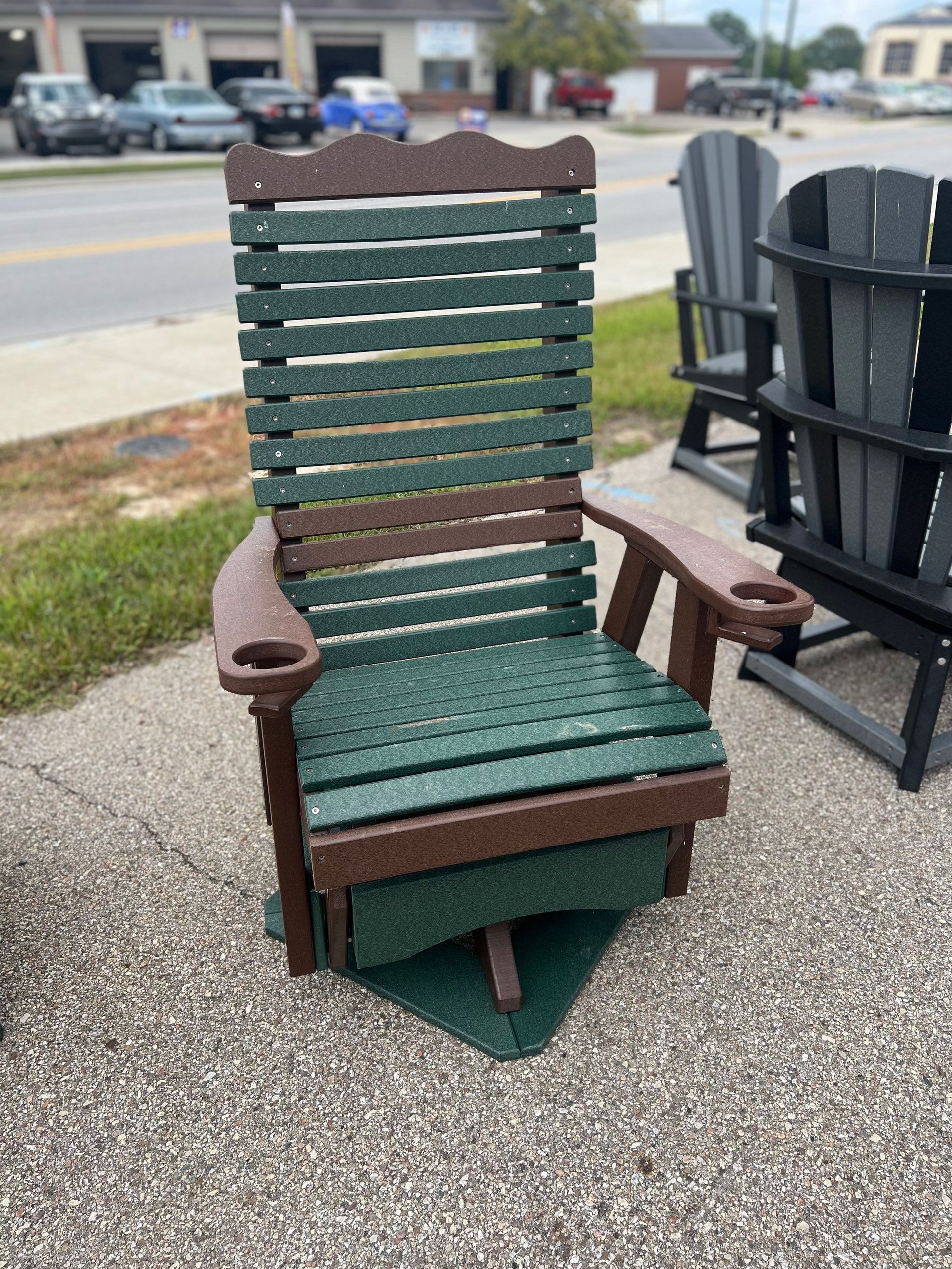 A green and brown rocking chair is sitting on a sidewalk.