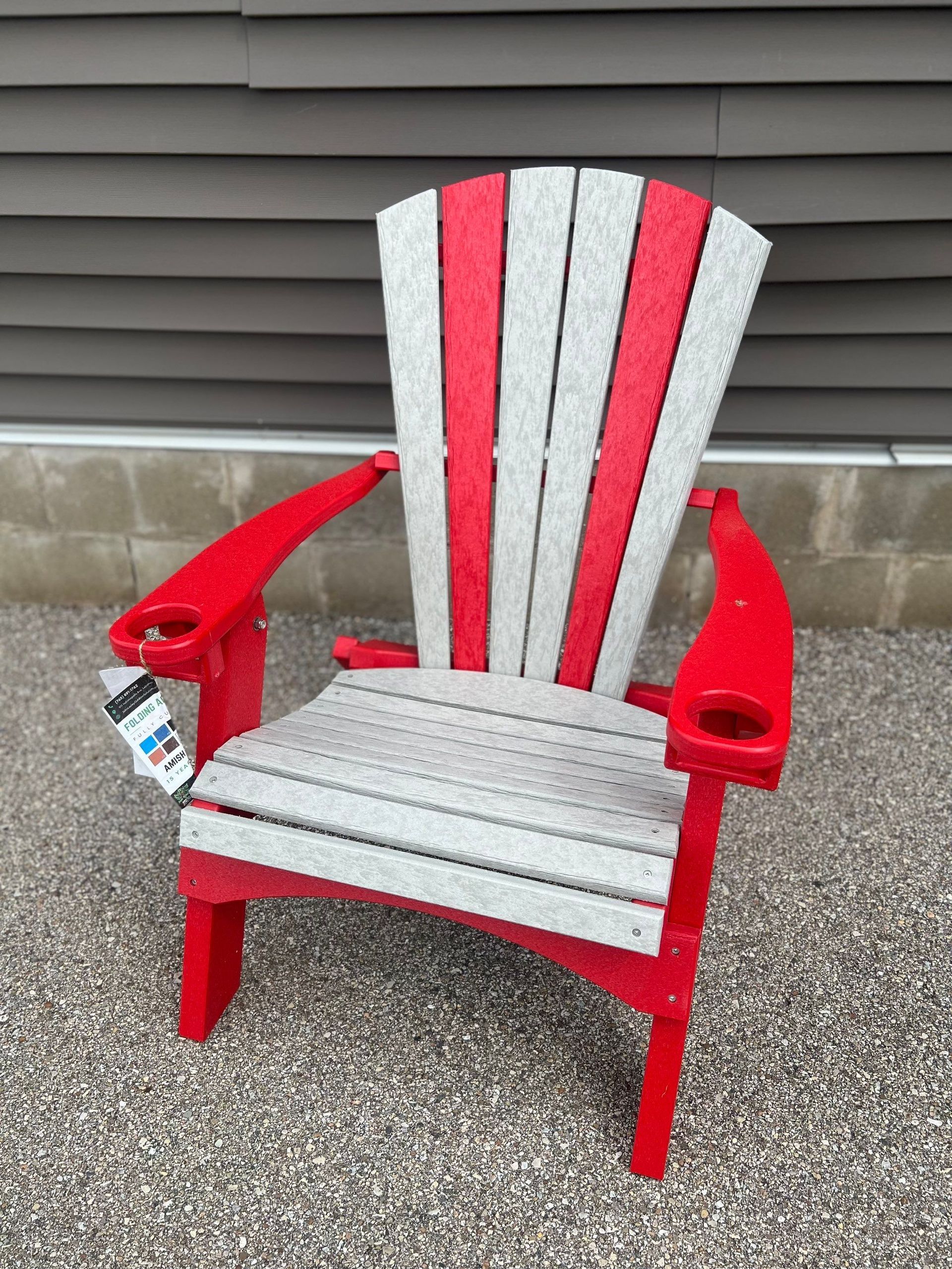 A red and white adirondack chair is sitting on gravel in front of a building.