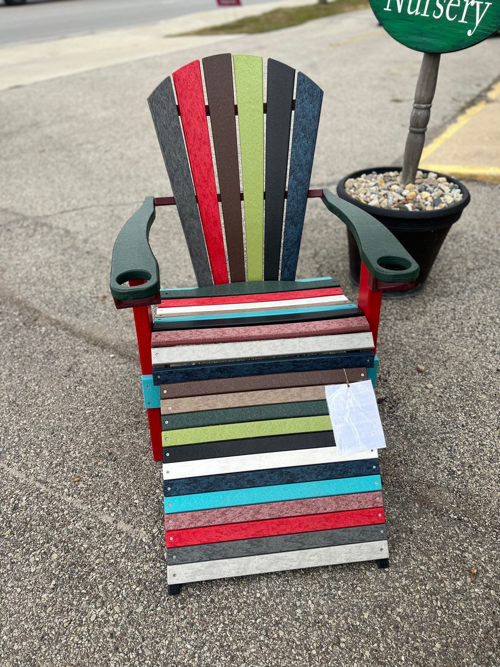 A colorful lawn chair is sitting on the side of the road next to a potted plant.