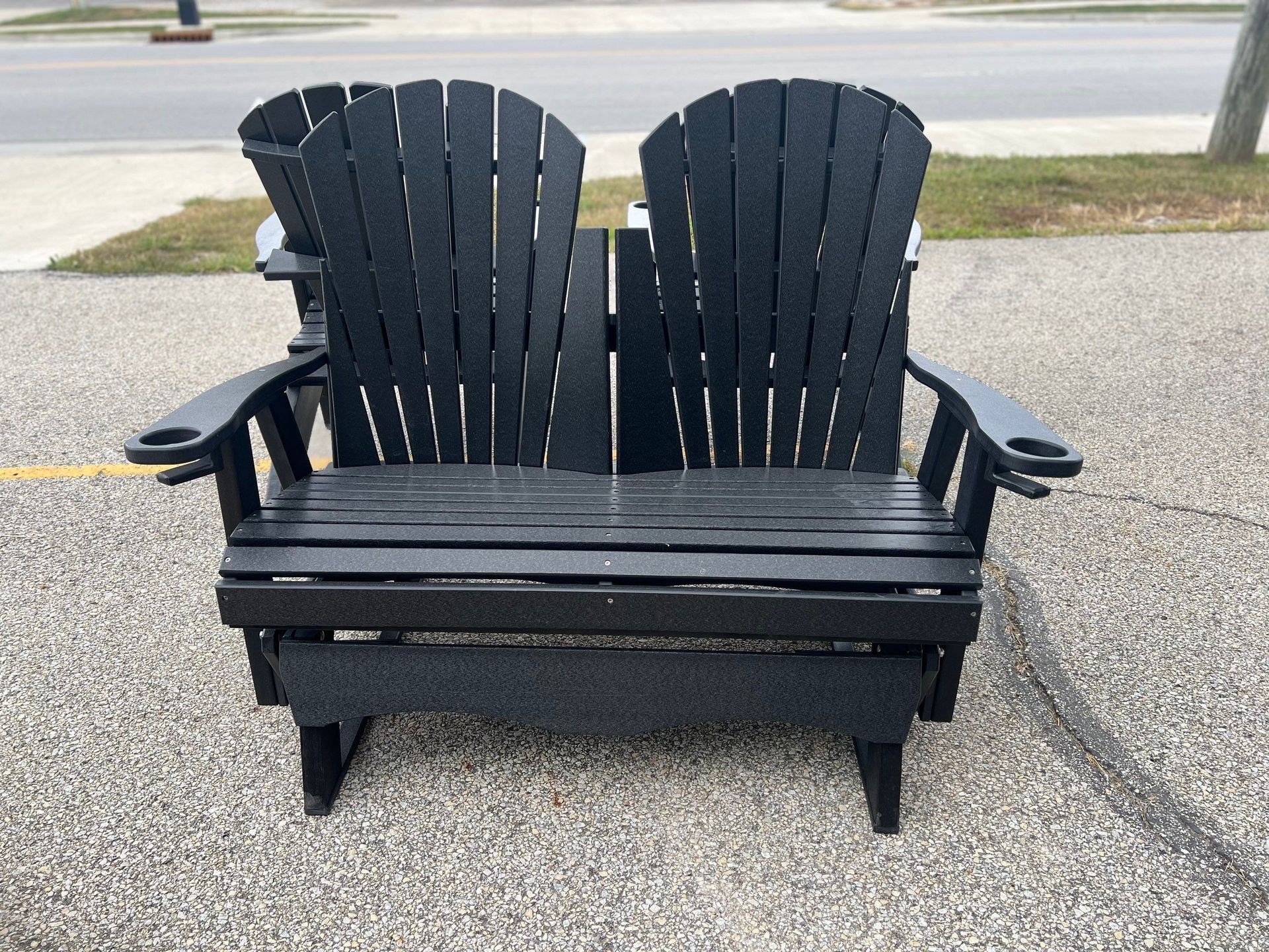 Two black adirondack chairs are sitting on a sidewalk