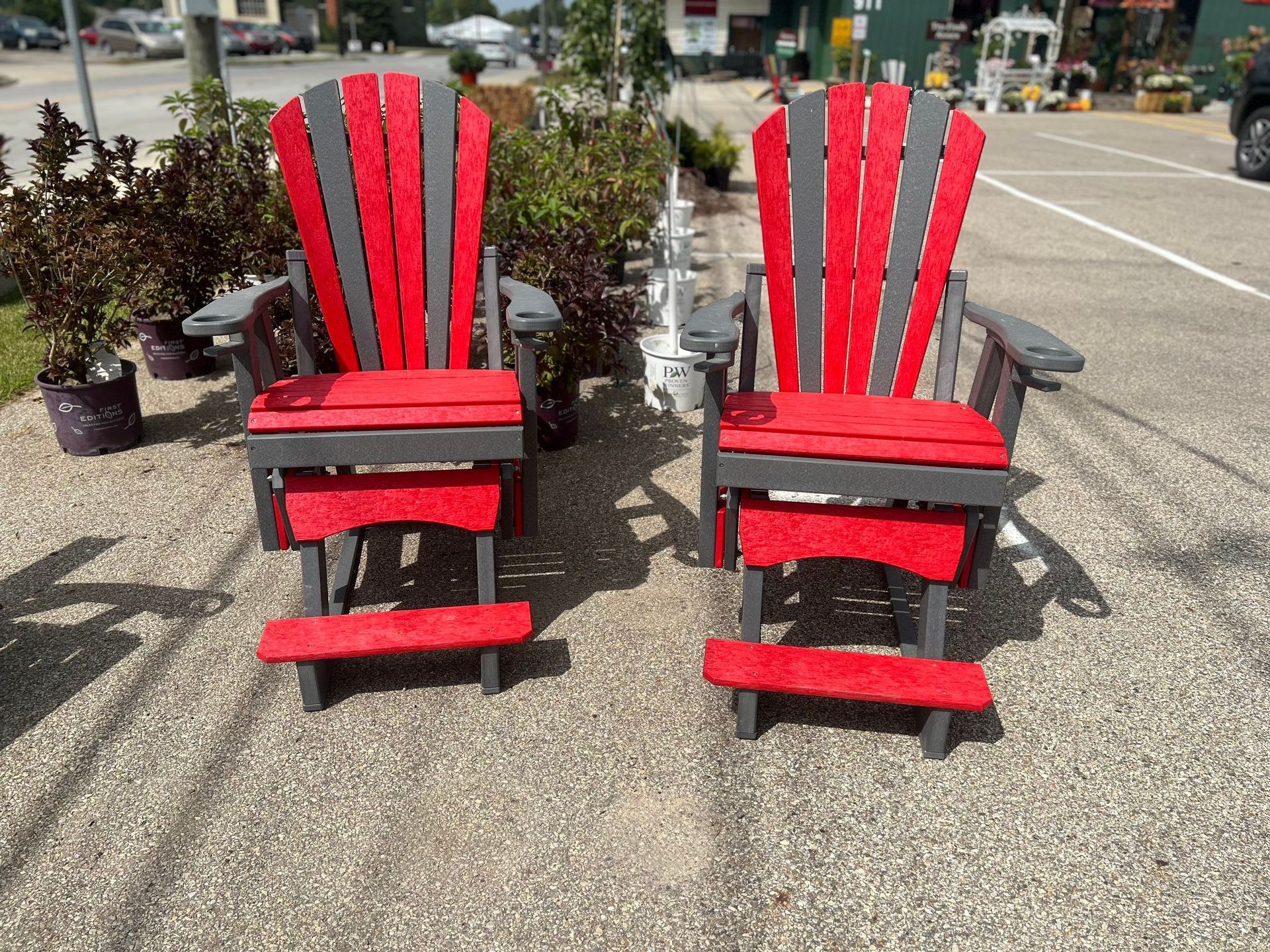Two red and gray adirondack chairs are sitting next to each other in a parking lot.