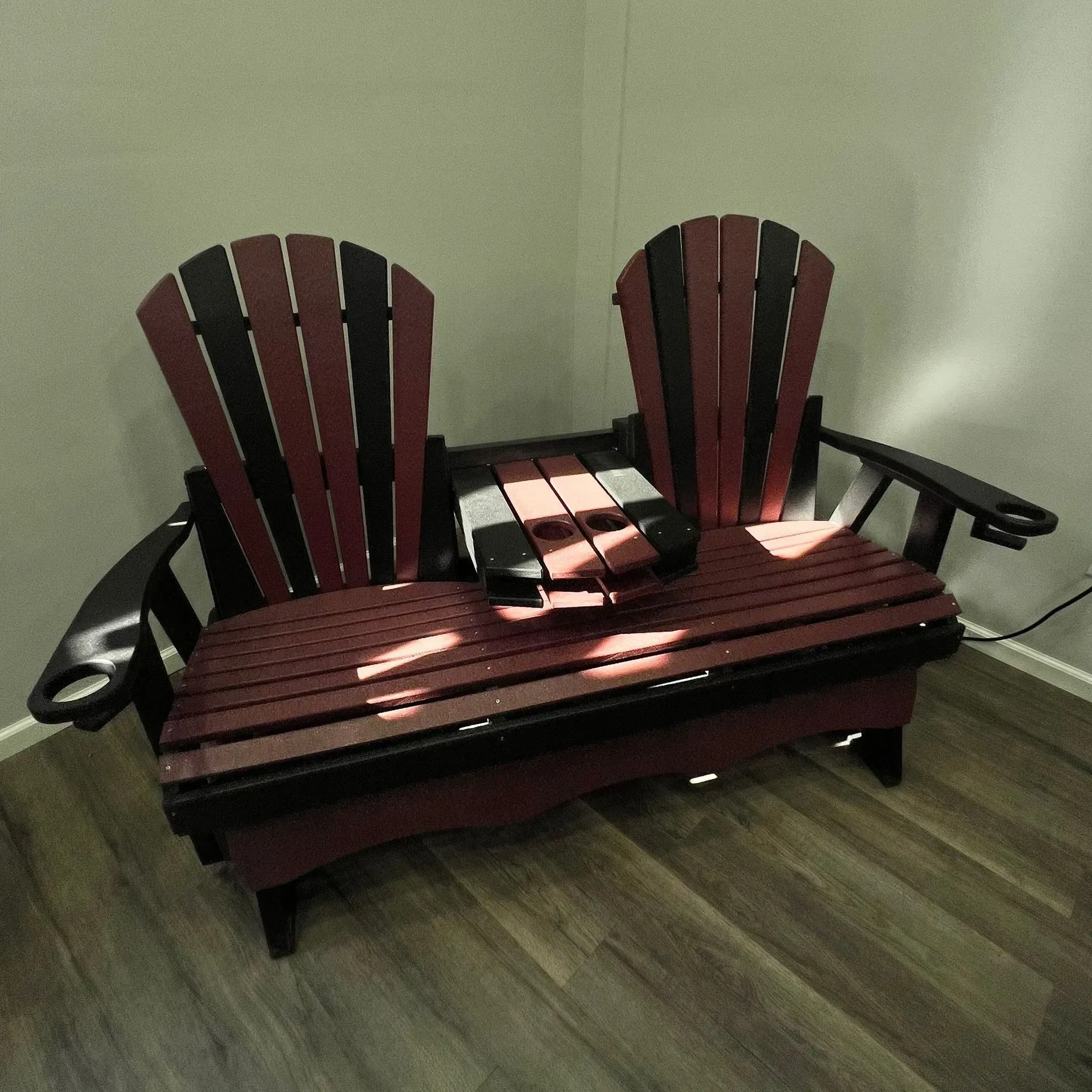 Two red and black adirondack chairs are sitting on a wooden bench