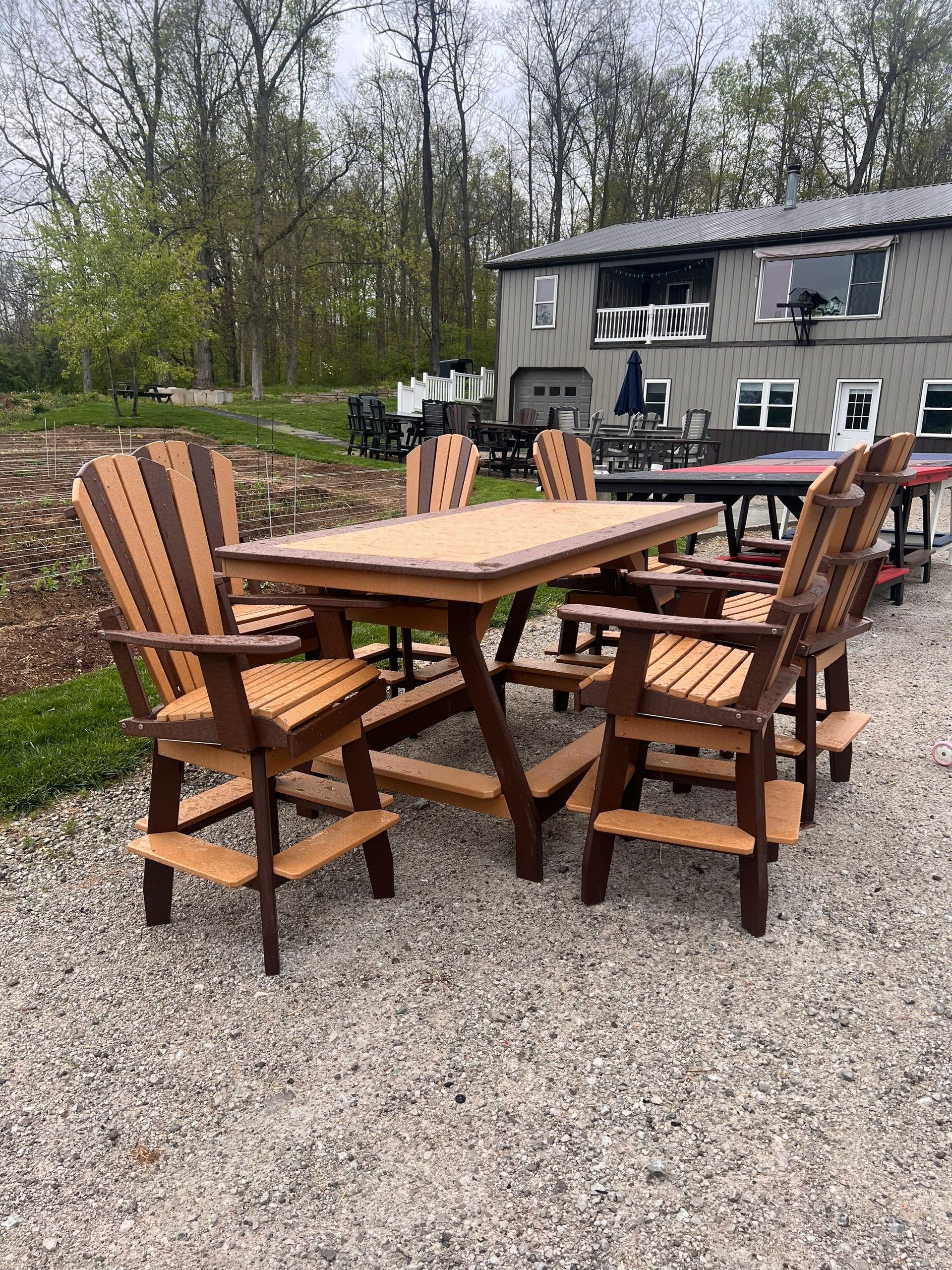A wooden table and chairs are sitting on gravel in front of a house.