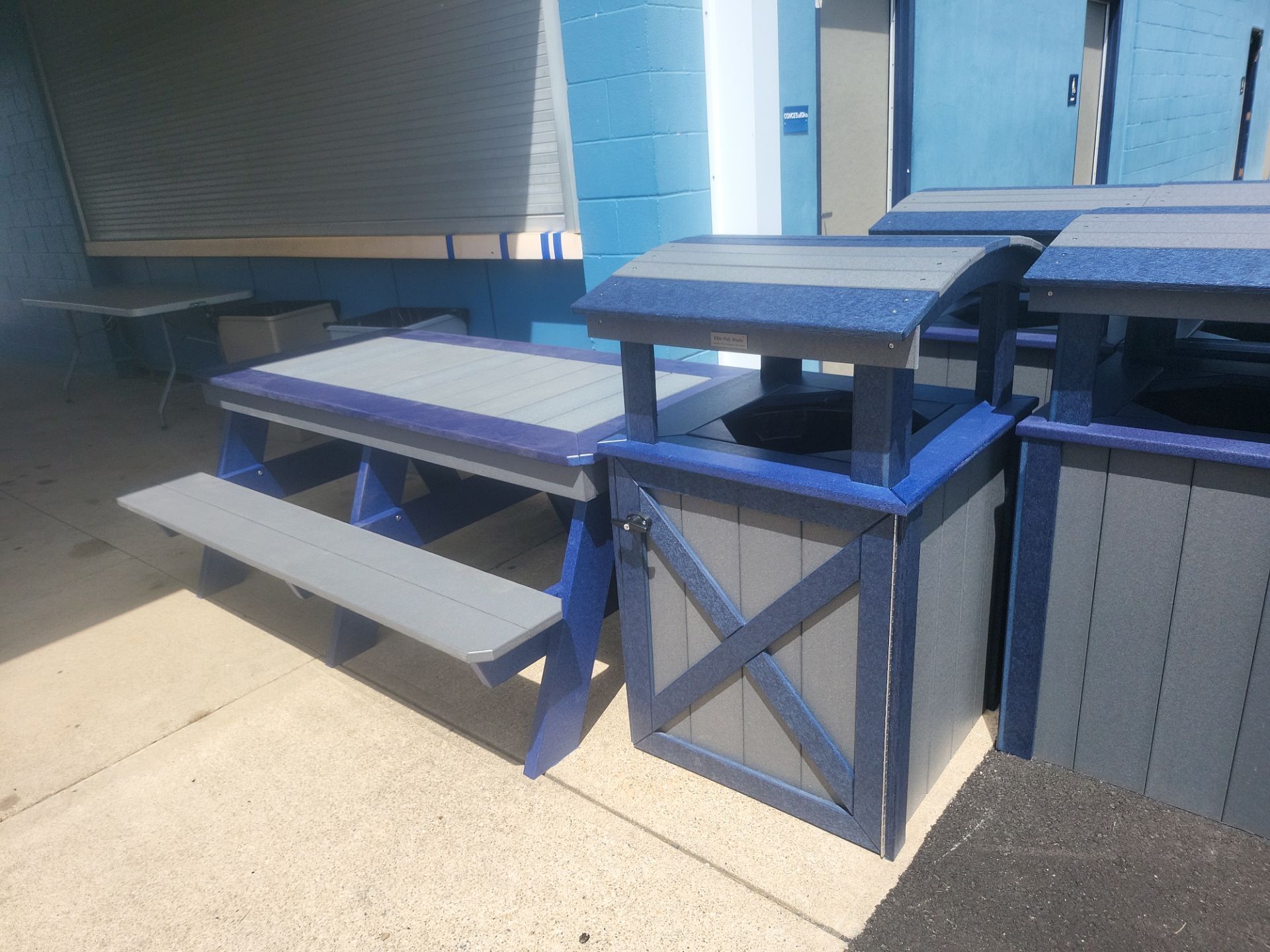 A row of blue and gray picnic tables and trash cans