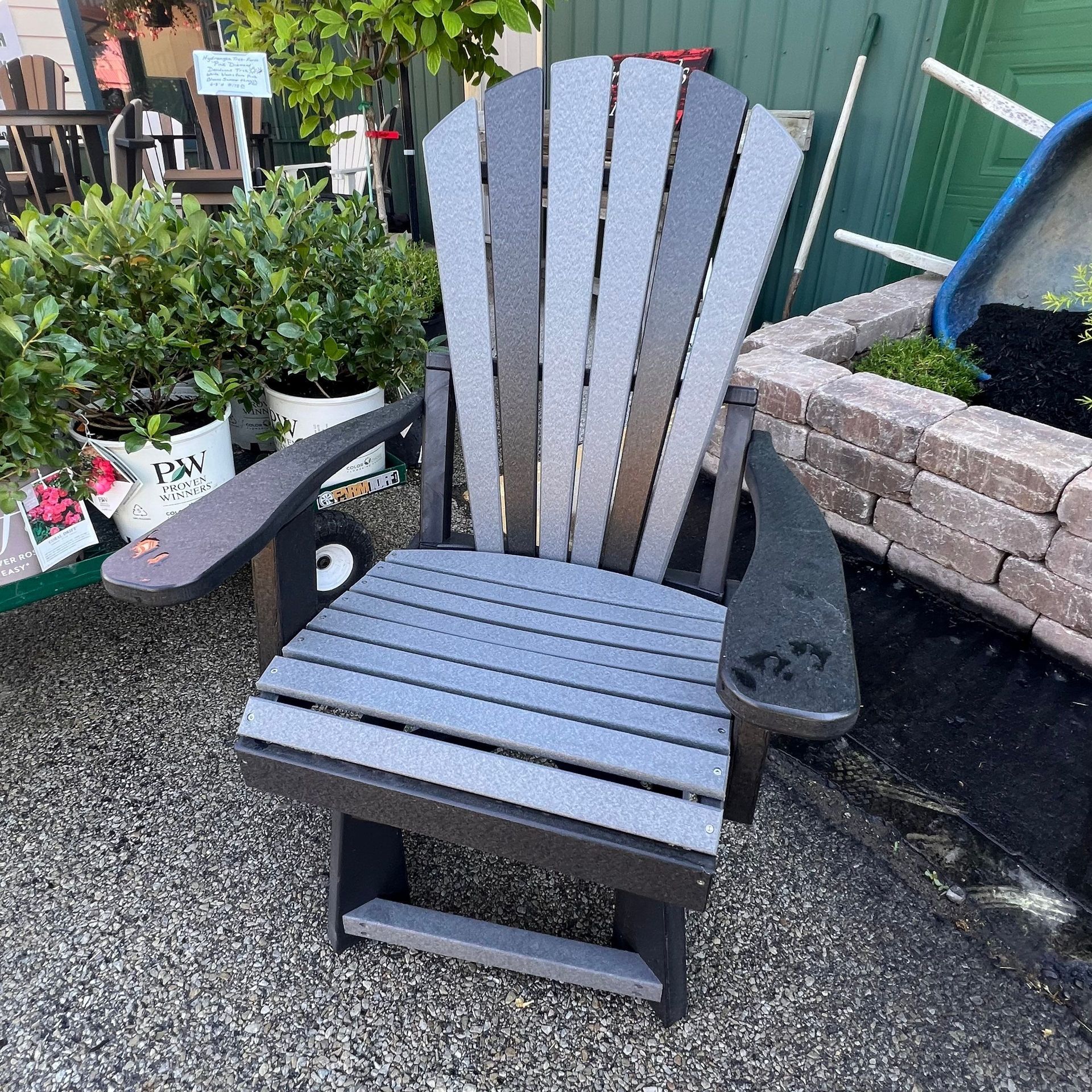 A gray and black adirondack chair is sitting on a gravel road.