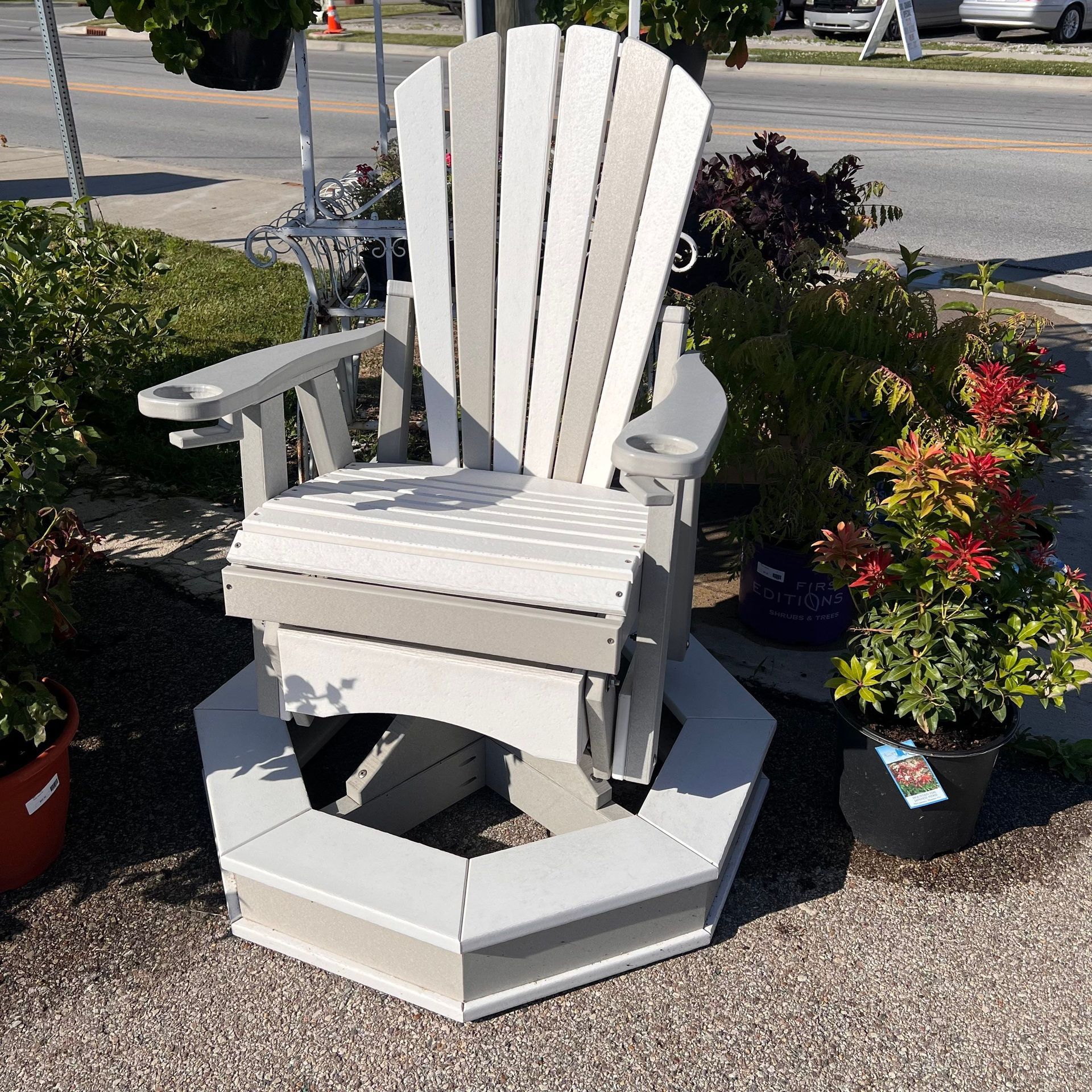 A white adirondack chair is sitting on the side of the road