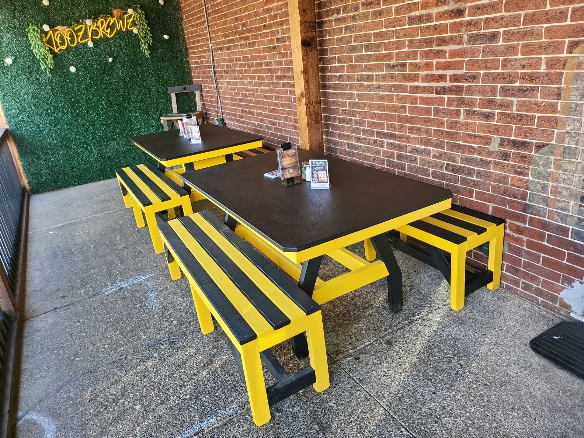 A yellow and black picnic table with benches in front of a brick wall.