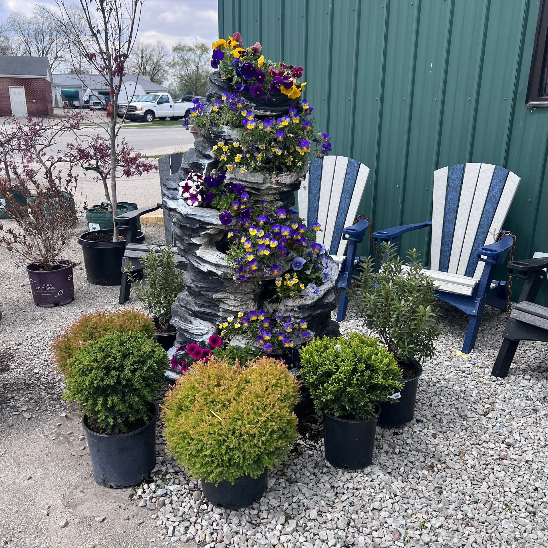 A stack of potted plants and chairs in front of a green building.