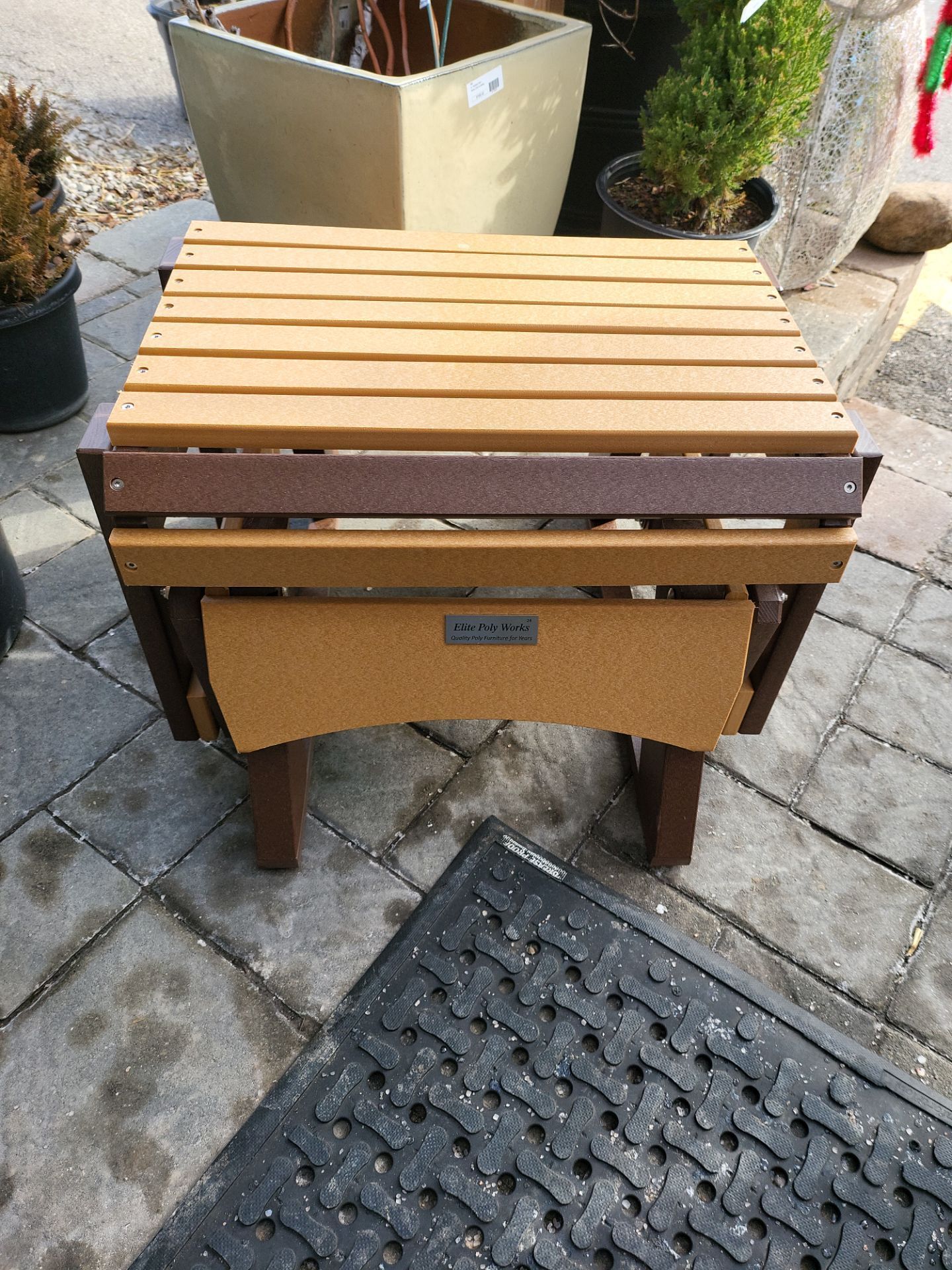 A wooden table is sitting on a brick sidewalk next to a black mat.