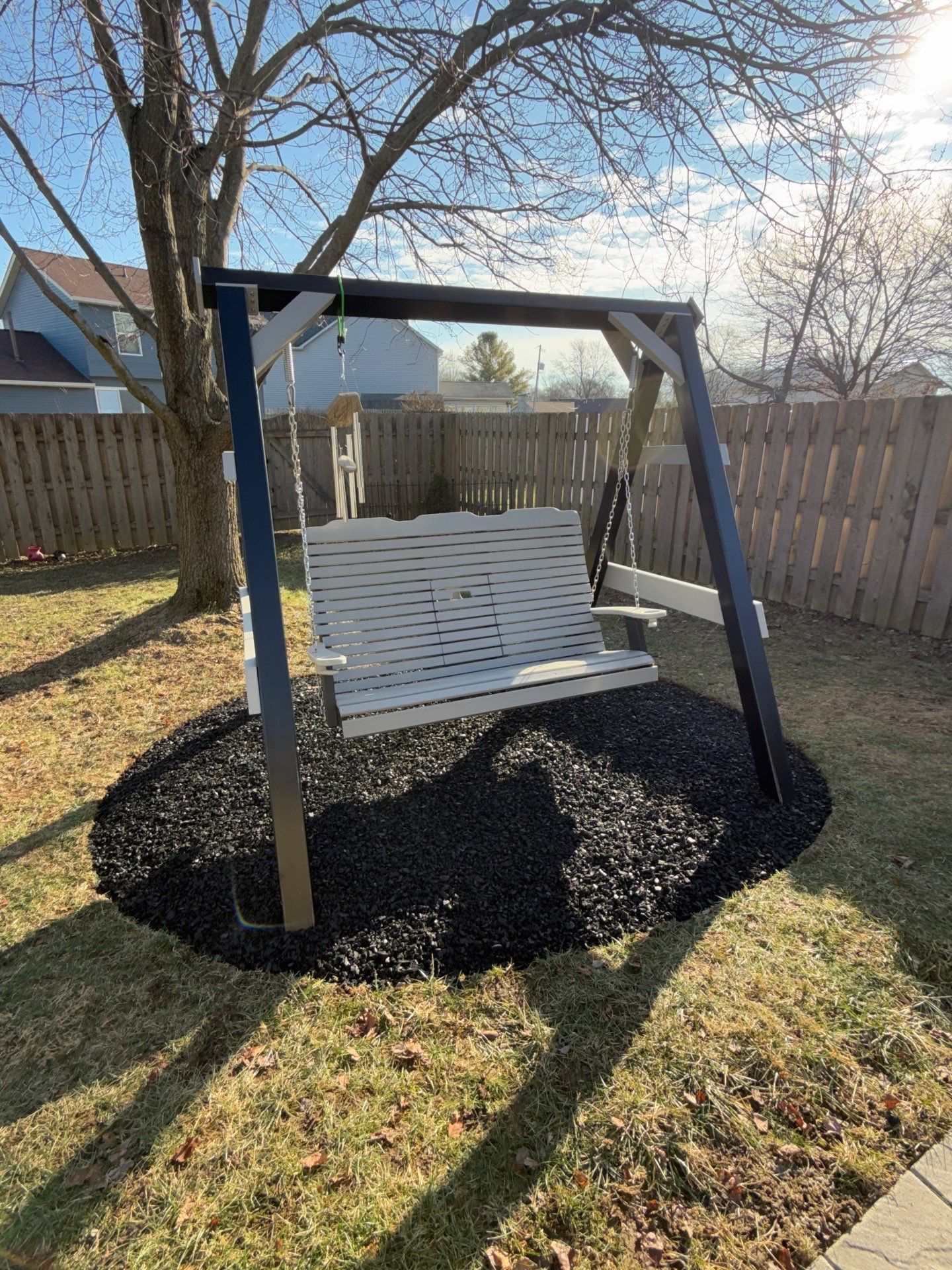 A white porch swing is sitting in the middle of a yard.