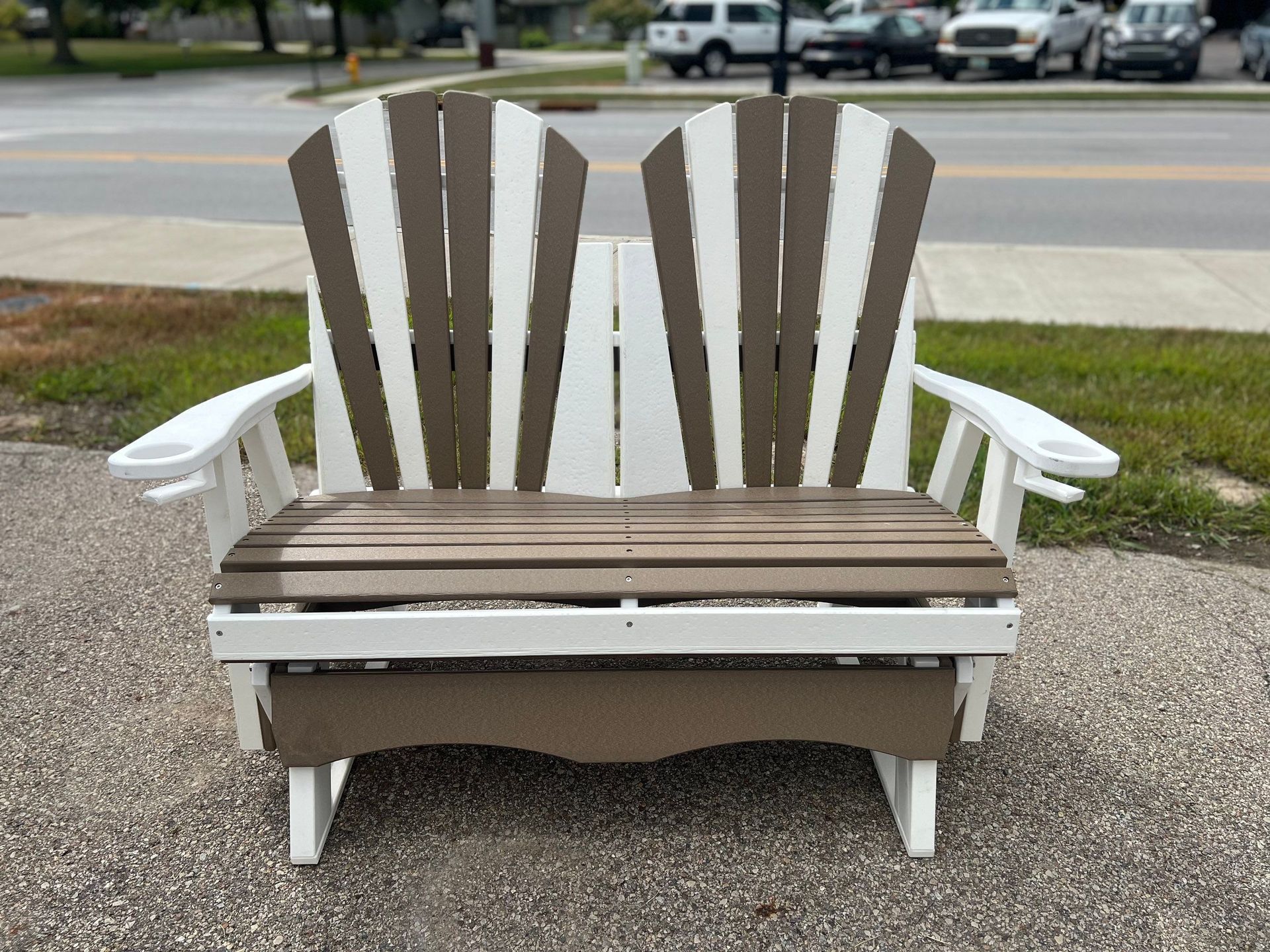 A brown and white wooden bench is sitting on the side of the road.