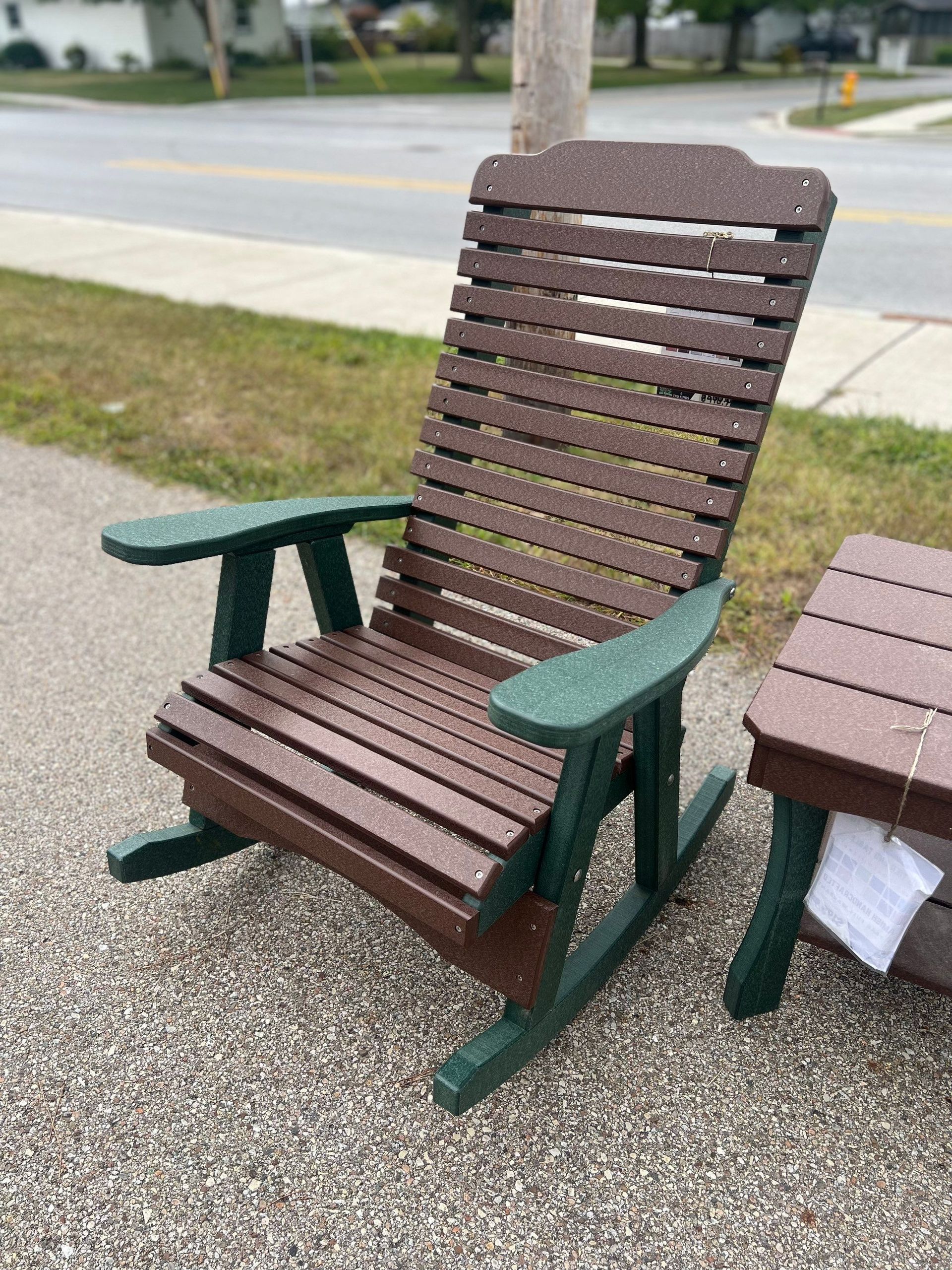 A wooden rocking chair is sitting on the sidewalk next to a table.