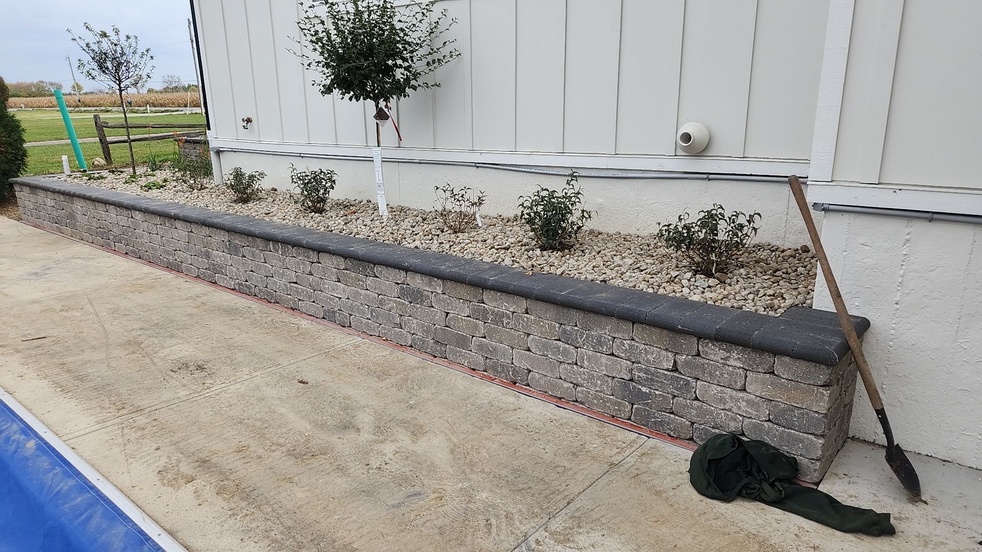 A rake is sitting on the sidewalk next to a stone wall.