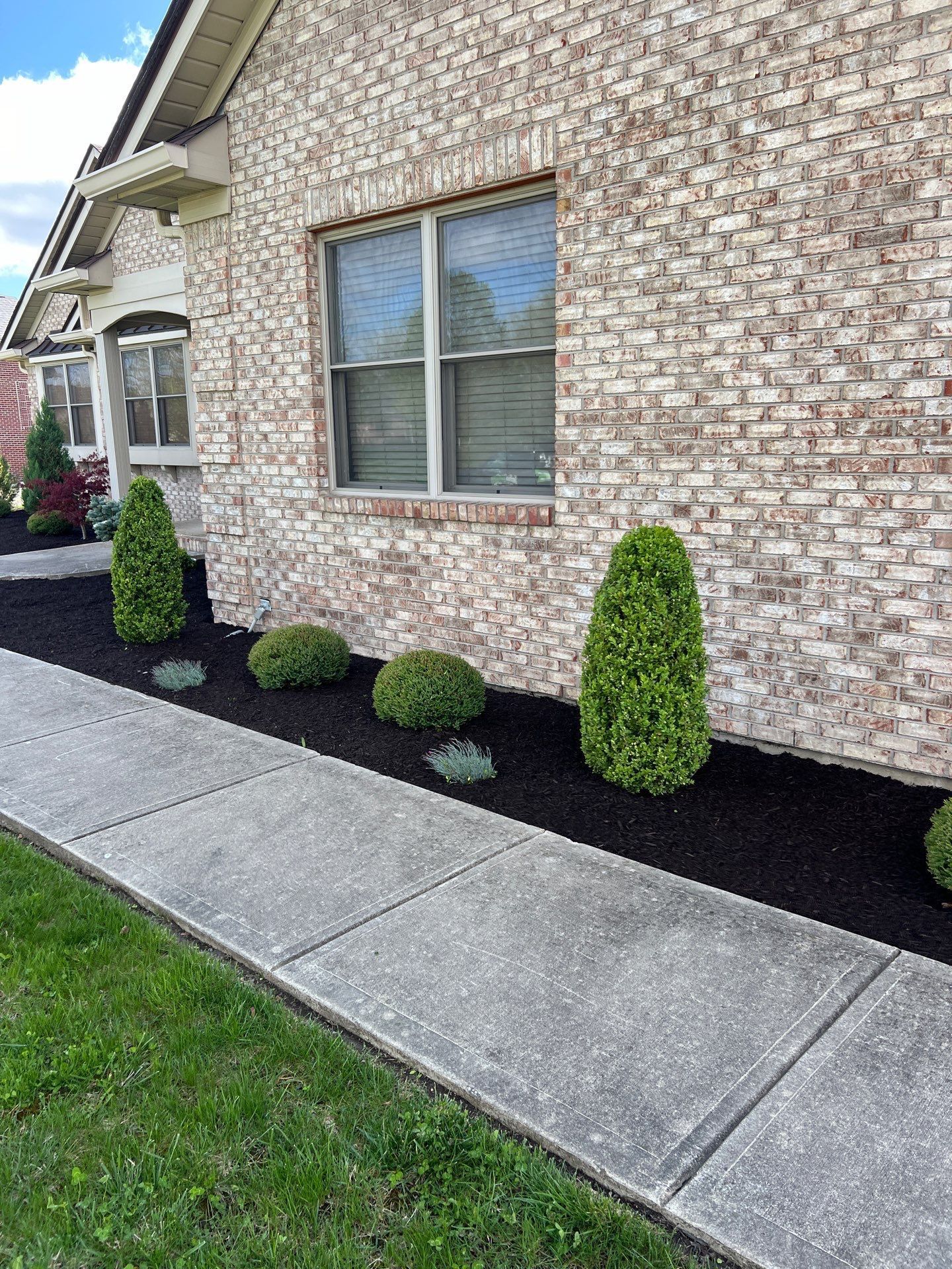 A brick house with a sidewalk and bushes in front of it.