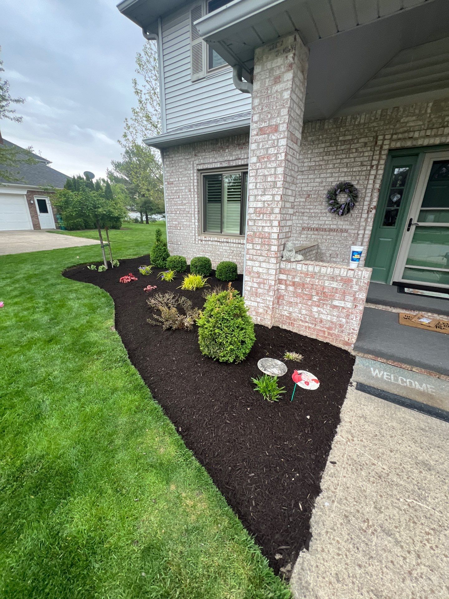 A house with a lush green lawn and mulch in front of it.