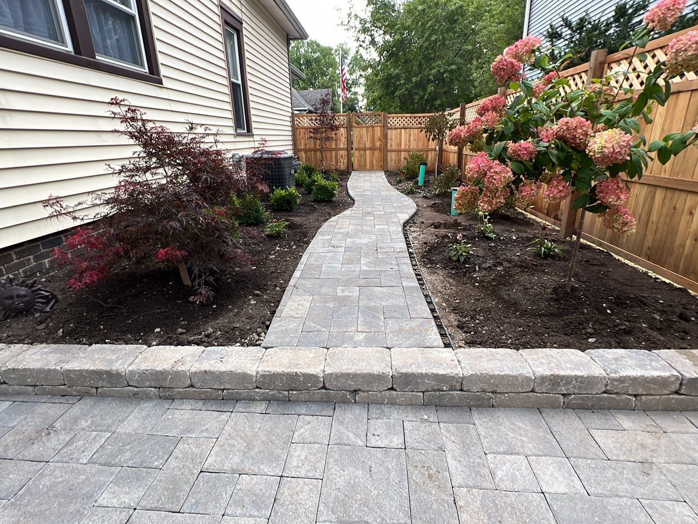 A walkway leading to a house with a wooden fence and flowers.