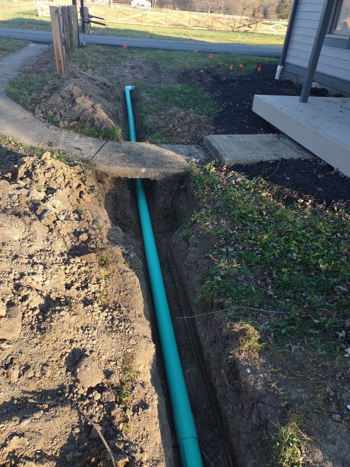 A green pipe is being installed in a trench in front of a house.