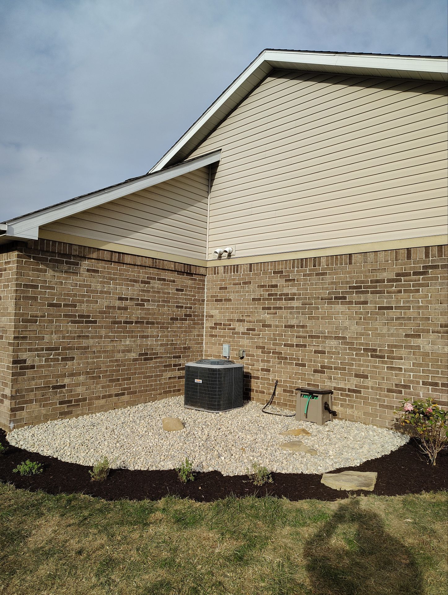 A house with a brick wall and a gravel area in front of it.