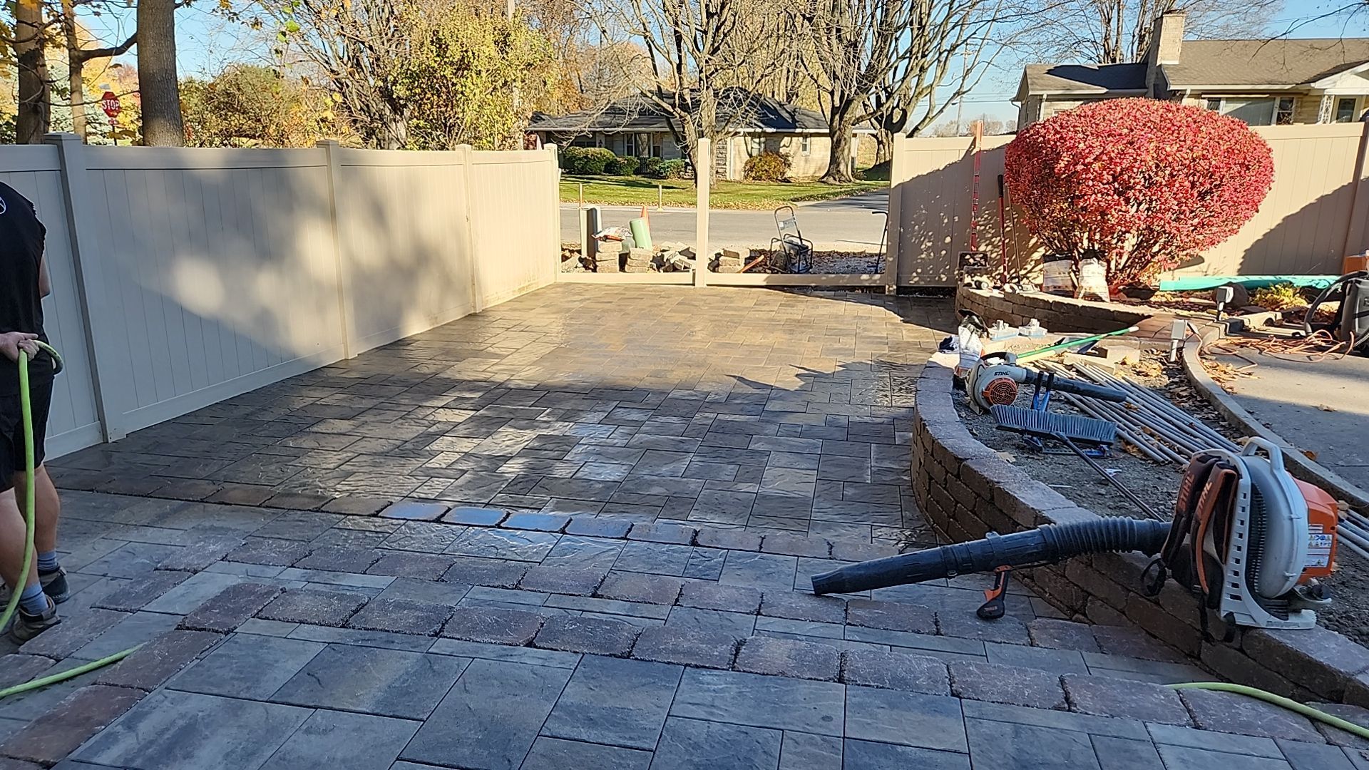 A man is standing next to a hose in a backyard.