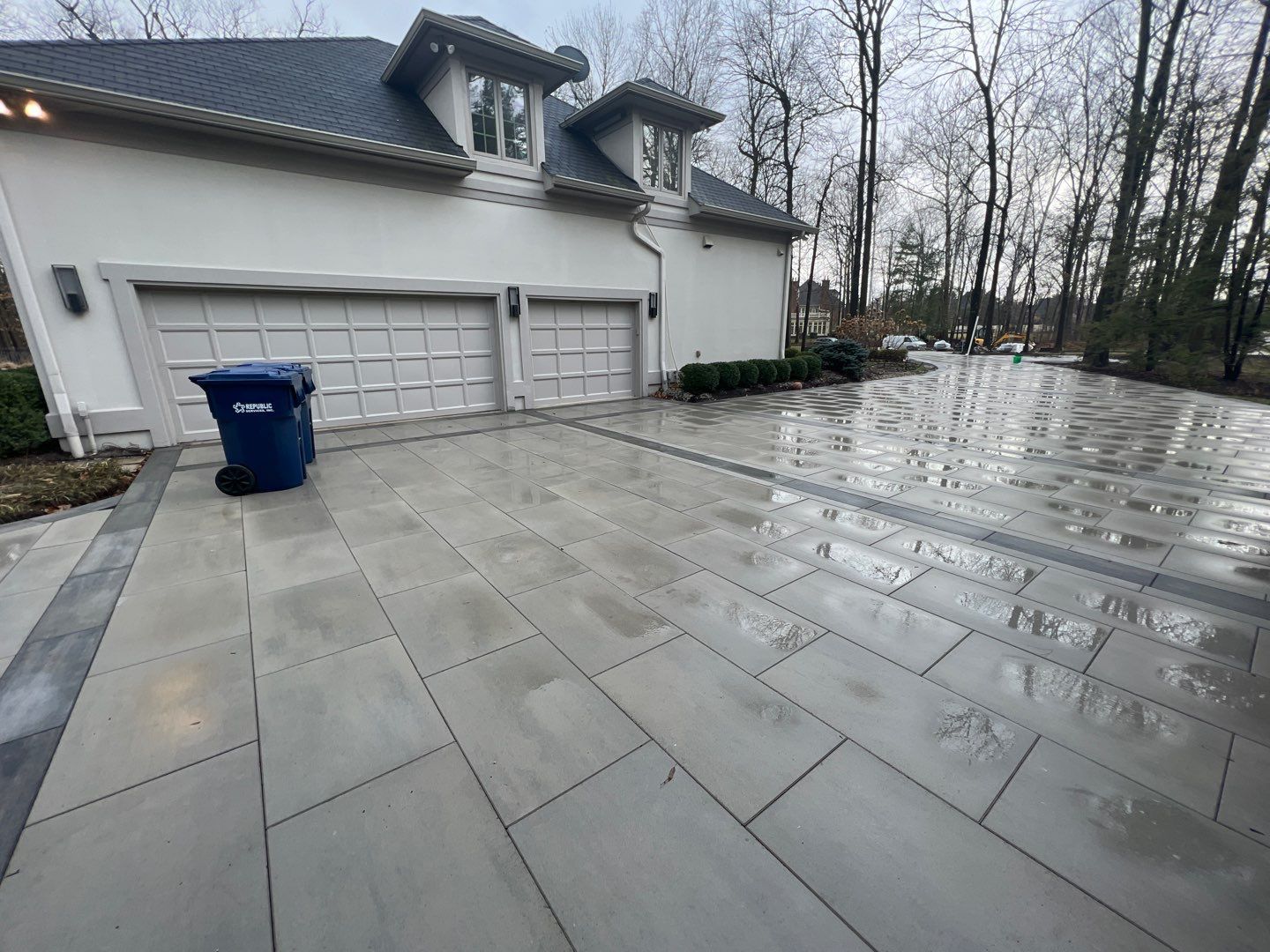 A large white house with a blue trash can in front of it.