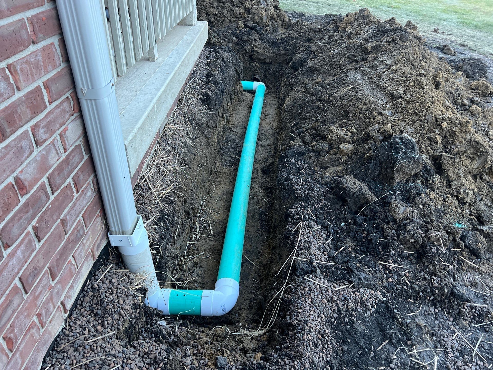 A green pipe is laying in the dirt next to a brick wall.