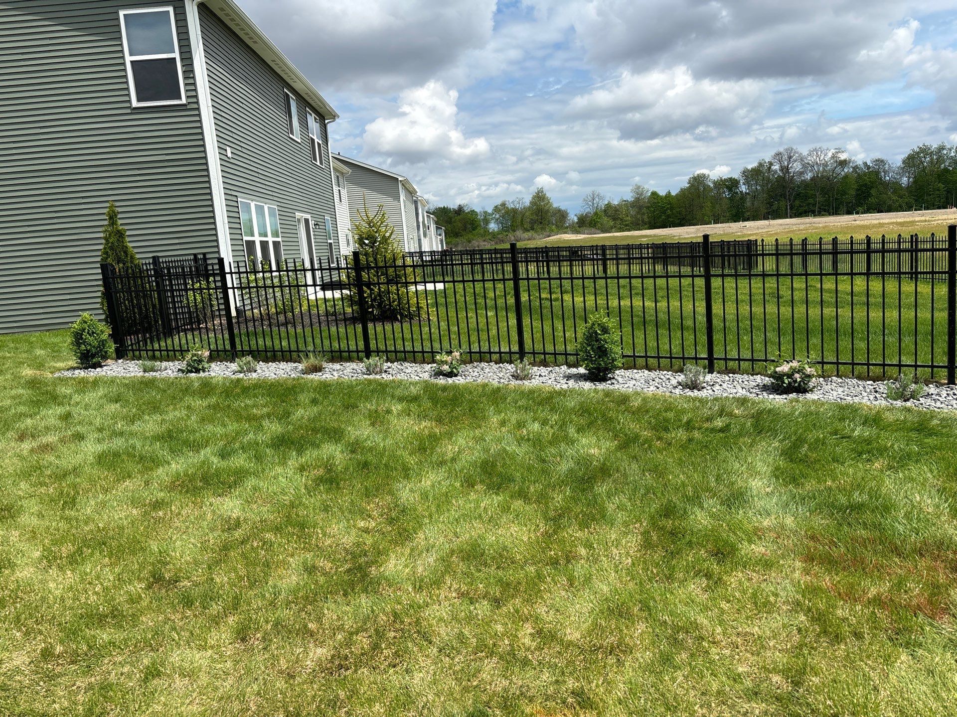 A black fence surrounds a lush green lawn in front of a house.